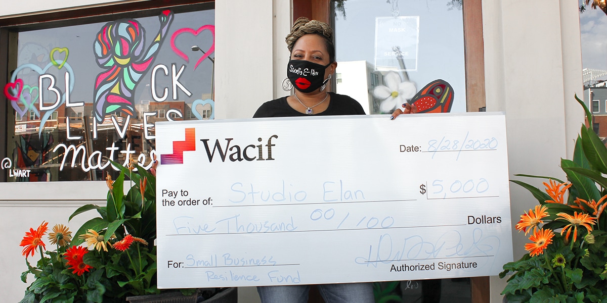 Photograph of woman of color entrepreneur holding a check from Wacif for $5,000